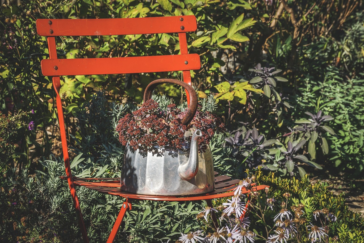 A red-orange garden chair holding a tin kettle spilling with sedum