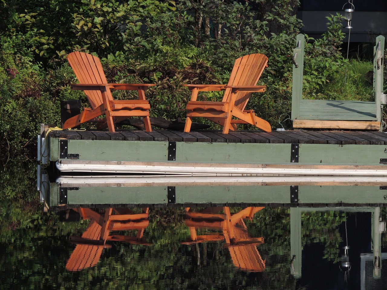 Two orange Adirondack chairs on a dock reflected in still water