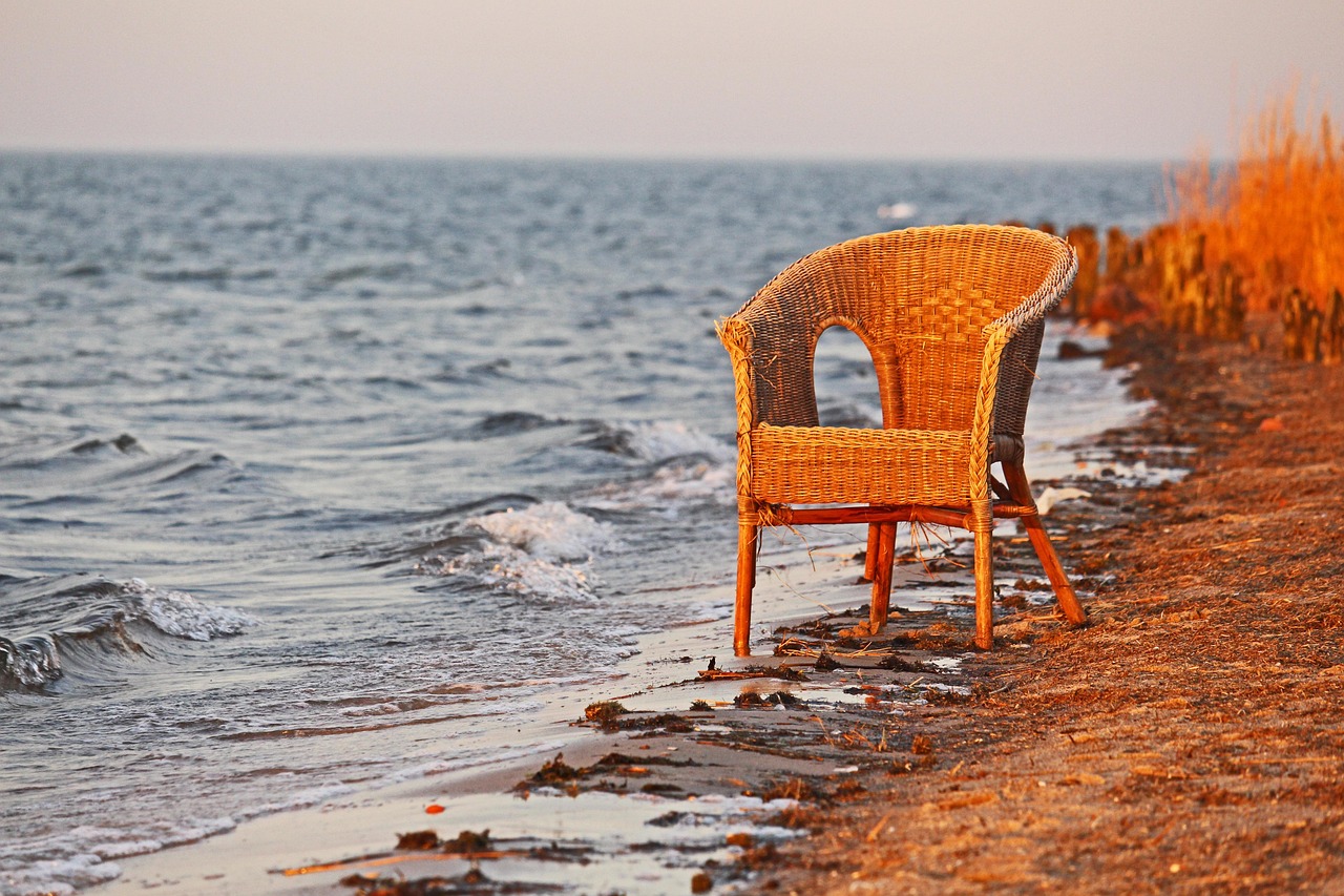 Weathered wicker chair at the water's edge at sunset